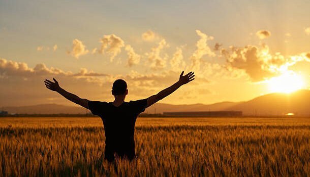 man with arms raised in wheat field posing in the sunset time with his arms raised.feeling complete.